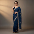 Shafusion blue georgette saree with intricate gold embroidery worn by a smiling woman in a studio setting.