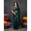 Shafusion green fox georgette solid saree with gold border and patterned blouse worn by a model among flower pots